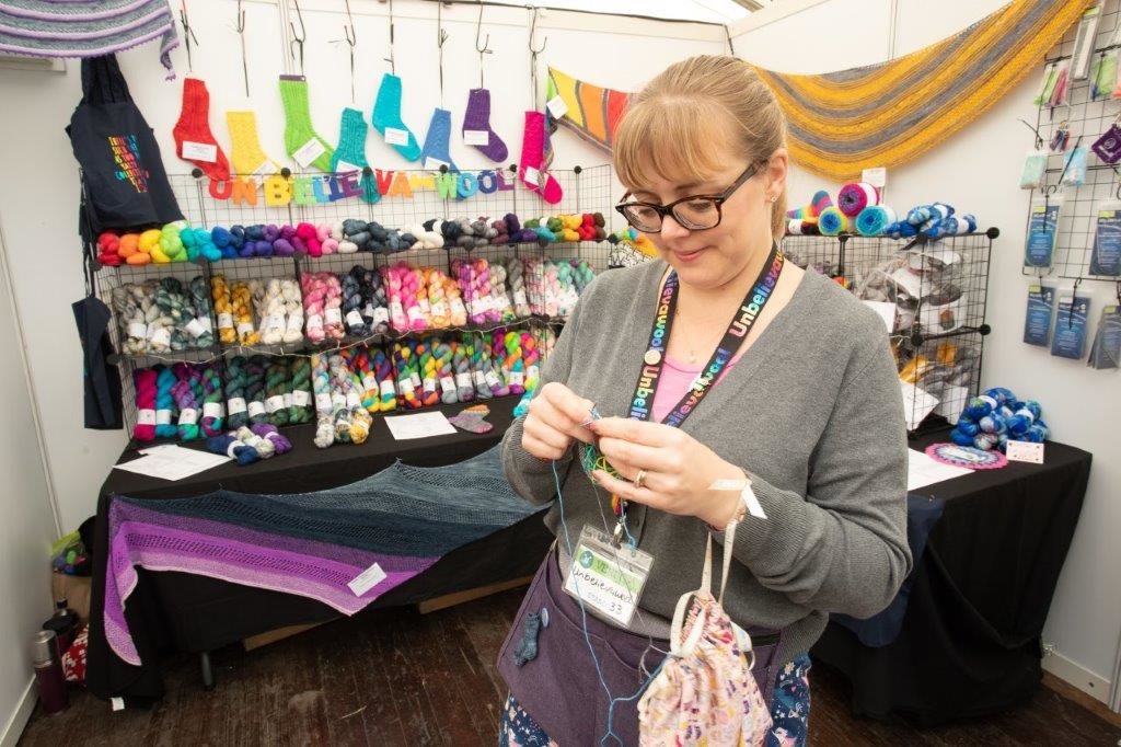 knitter working on knitting project in front of vendor booth at woollinn yarn festival