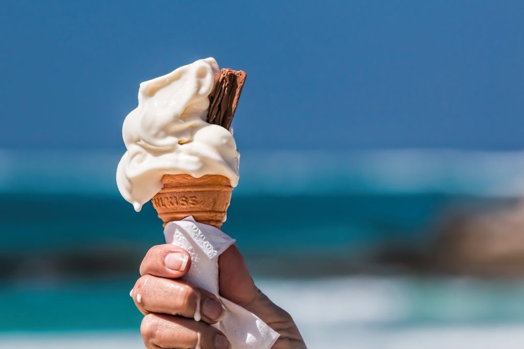hand holding vanilla ice cream cone with chocolate flake with sea in background